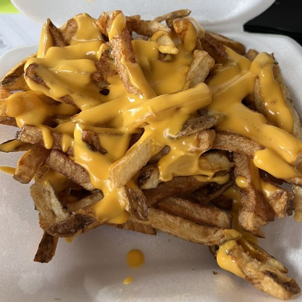 A close-up of golden-brown french fries generously covered with melted yellow cheese sauce in a white container.