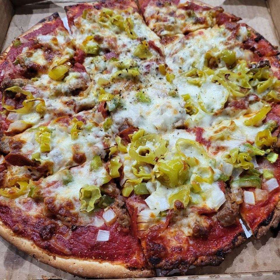 A Chicago-style pizza with melted cheese, green peppers, and sausage in a cardboard box.