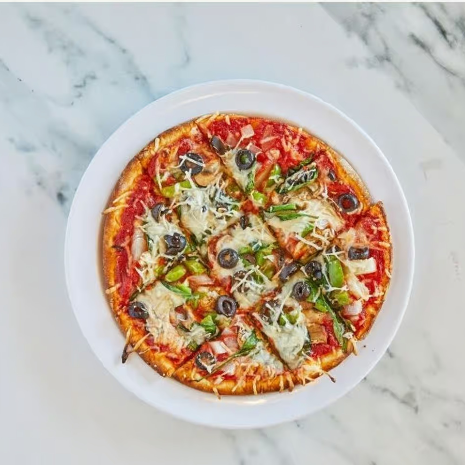 A sliced Windy City Chicago Style Pizza with olives, green peppers, and cheese on a white plate.