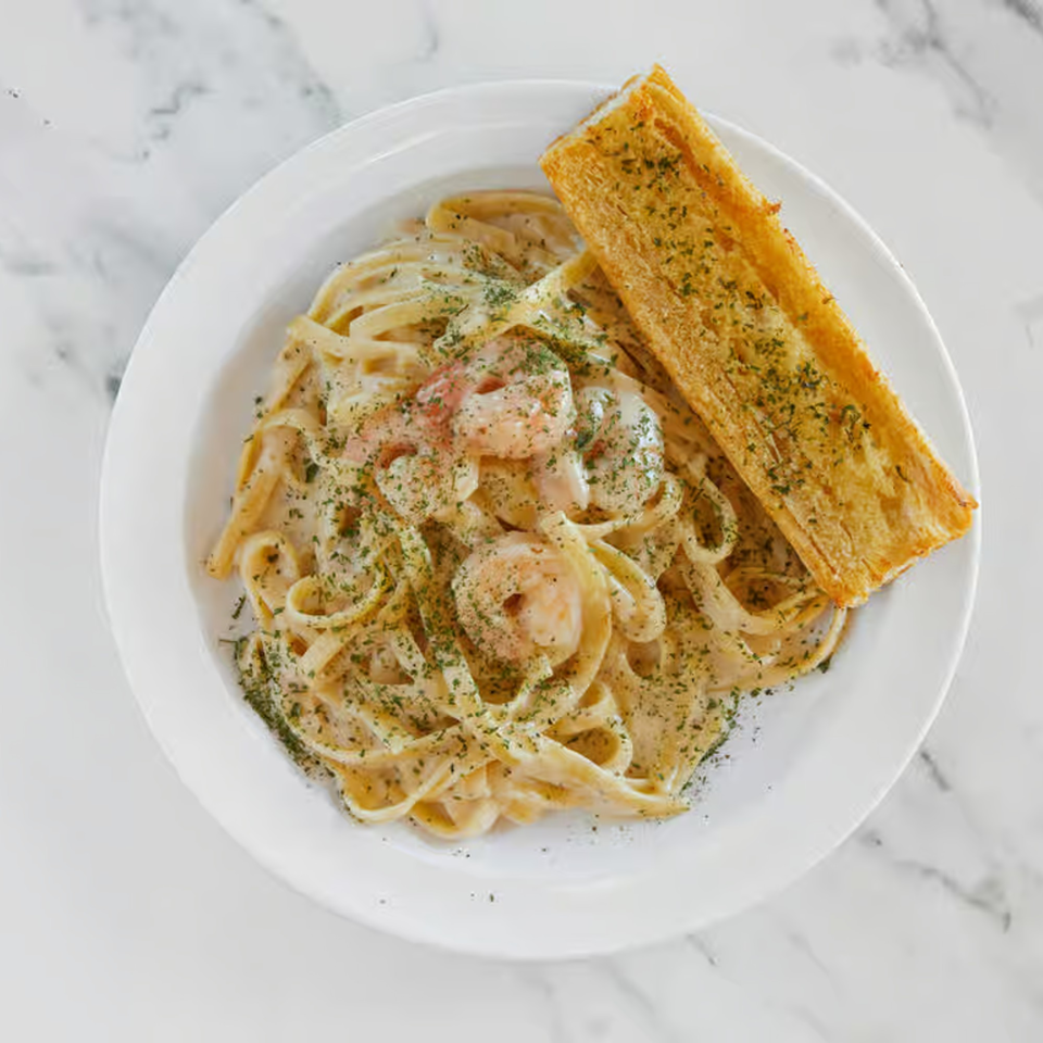 Creamy shrimp fettuccine pasta with parsley and a side of garlic bread on a white plate.