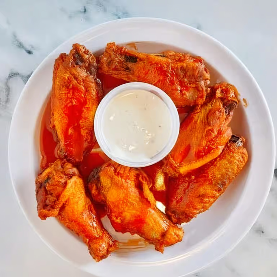 A white plate of Windy City Chicago Style Pizza's buffalo wings with a side of ranch dressing.